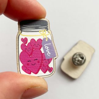Close up of wooden 'Love in a Jar' pin badge held in a hand