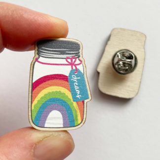 Close up of wooden 'Dreams in a Jar' pin badge held in a hand